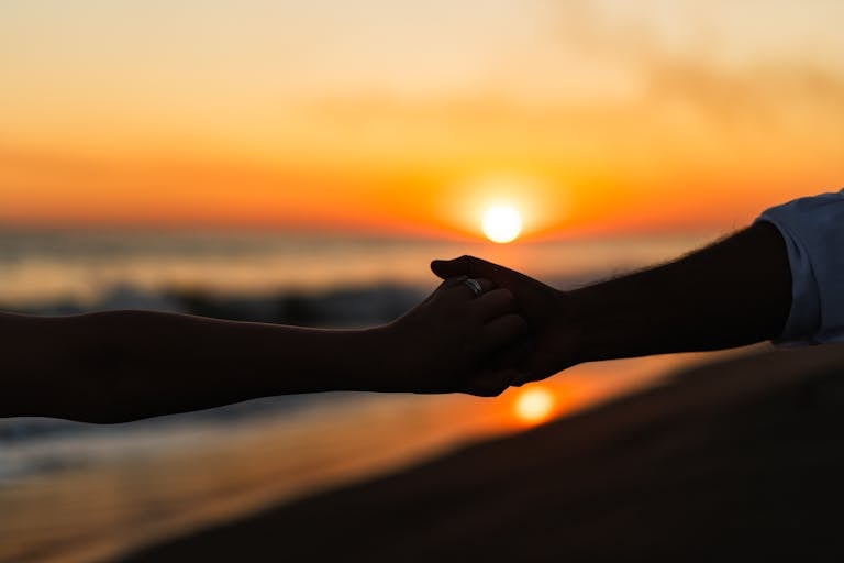 Silhouetted couple holding hands at sunset on a tranquil beach.