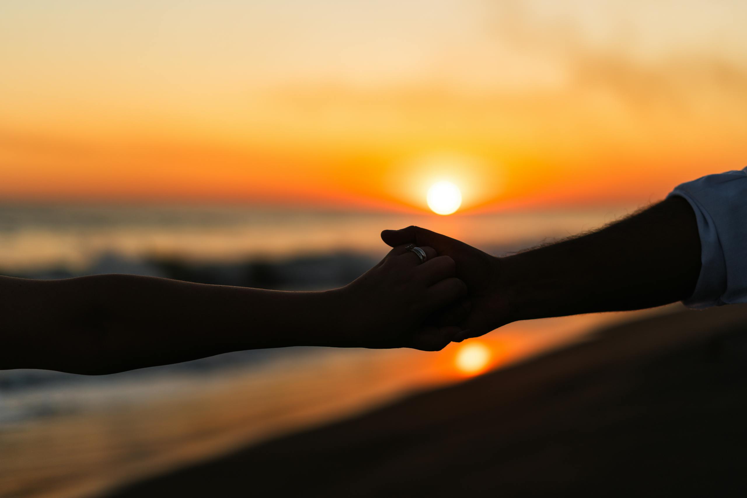 Silhouetted couple holding hands at sunset on a tranquil beach.