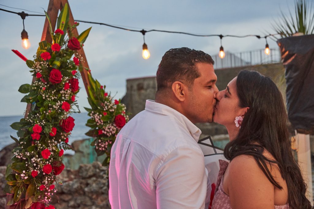 Pareja besándose bajo un arco de rosas rojas frente al mar